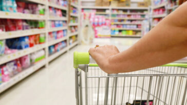 woman's hand on shopping trolley in supermarket aisle