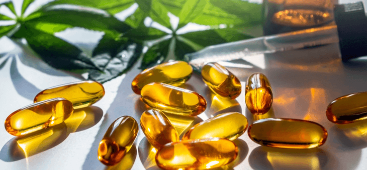 cannabis oil capsules and dropper in front of cannabis leaves