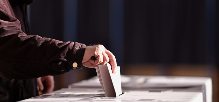 man placing paper vote in voting box