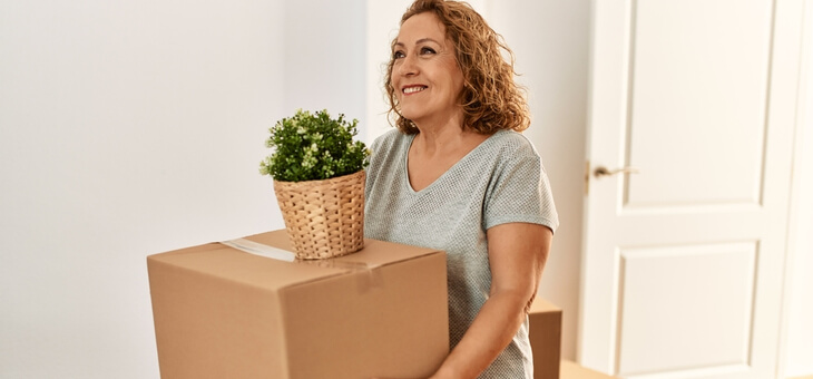 middle aged woman moving box and pot plant into new house