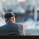 elderly man in peaked cap sitting along on bench