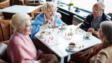 group of four elderly women at a table playing cards