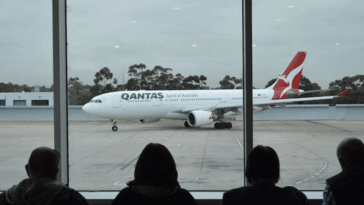 group of people in airport watching qantas plane taxiing