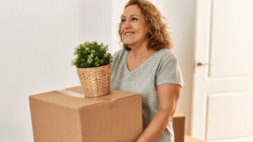 middle aged woman moving box and pot plant into new house