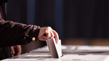 man placing paper vote in voting box