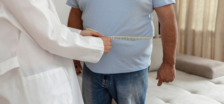 overweight man having belly measured by doctor