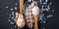 one wooden spoon filled with pink rock salt and another filled with white rock salt