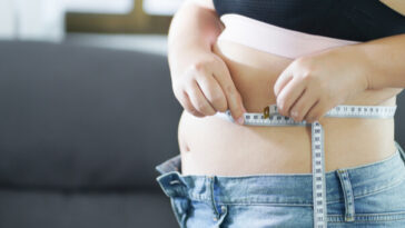 overweight woman measuring belly with tape measure