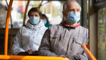 man and woman on bus both wearing masks
