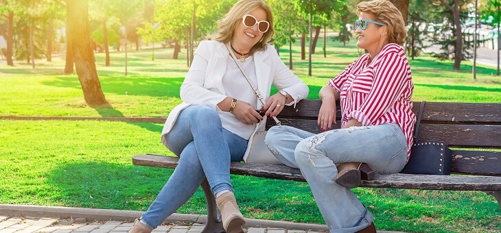 two women sitting on park bench wearing jeans