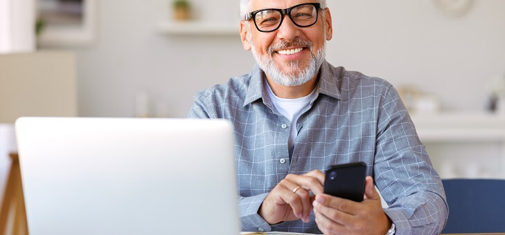 smiling older man using phone and laptop