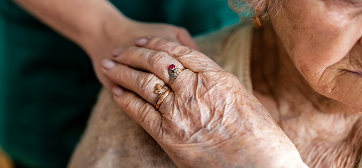elderly woman in care home with nurse's hand on shoulder