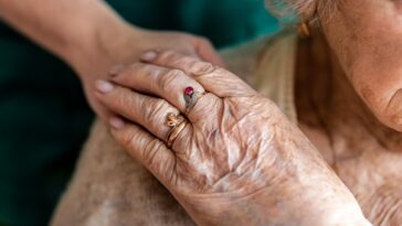 elderly woman in care home with nurse's hand on shoulder