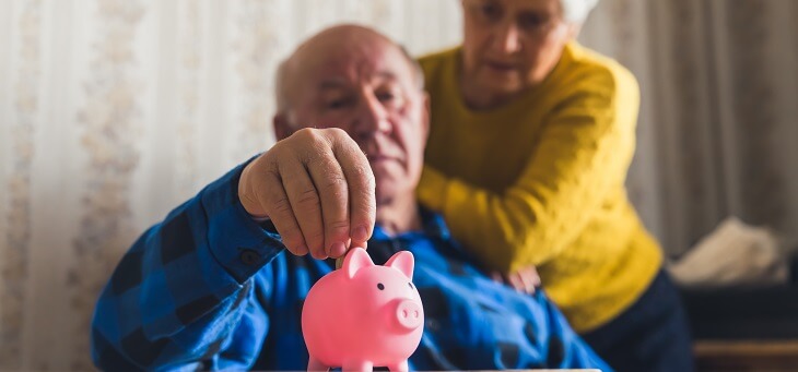 senior couple placing coins in piggy bank
