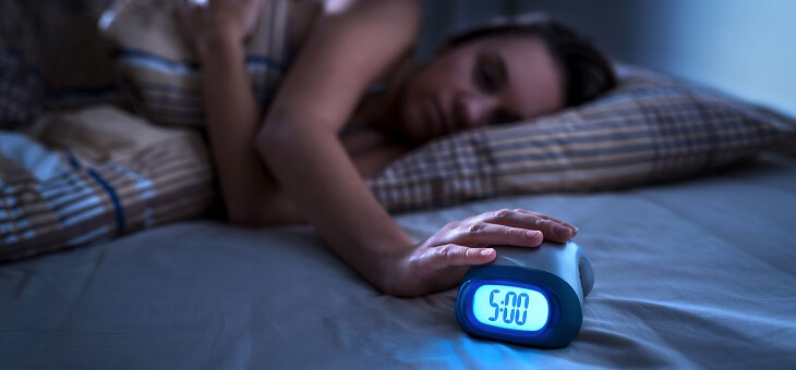 woman reaching for alarm clock from bed