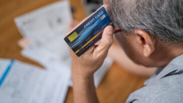 stressed elderly man looking at bills holding credit card