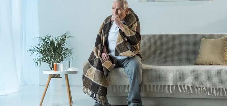 senior man coughing and wrapped in blanket