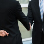 two businessmen in suits shaking hands with fingers crossed