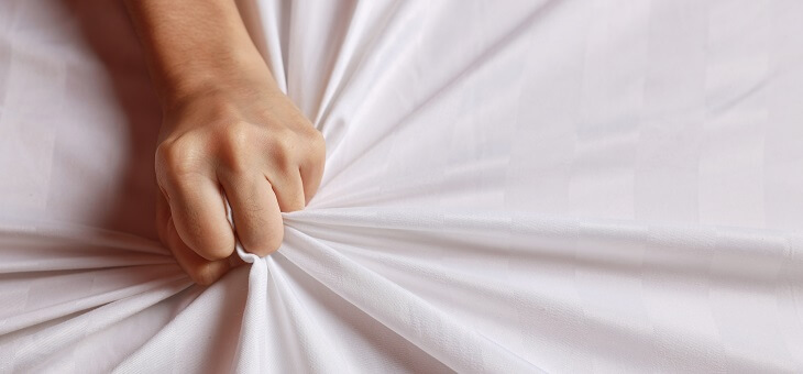 woman's hand gripping bedsheet tightly