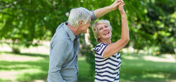 happy retired couple dancing in park