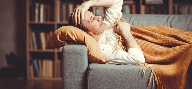 sick man lying on couch under blanket