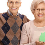 smiling elderly couple holding model house