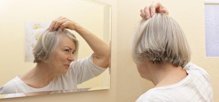older woman looking at her thinning hair in mirror