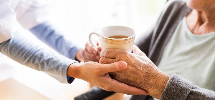 nurse giving cup of tea to resident in aged care home