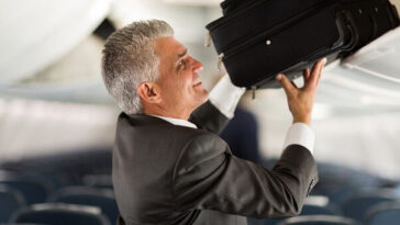 man putting luggage in overhead compartment