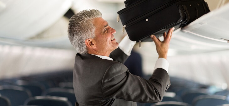 man putting luggage in overhead compartment