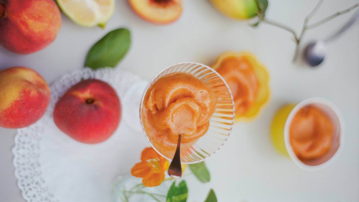 Orange sorbet in a glass surrounded by peaches