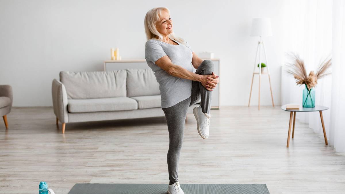 Woman exercising standing on a yoga mat, pulling her knee to her chest