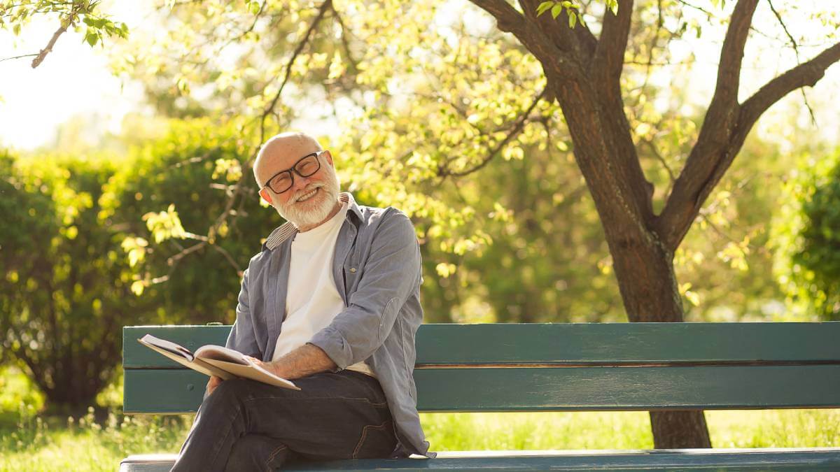 Older man reading on park bench, looking happy