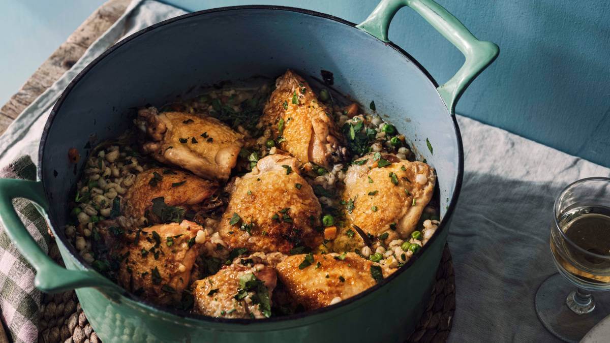 Chicken thighs in a pot with with pearl barley, white wine and peas.