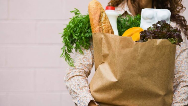 Woman clutching paper bag full of groceries.