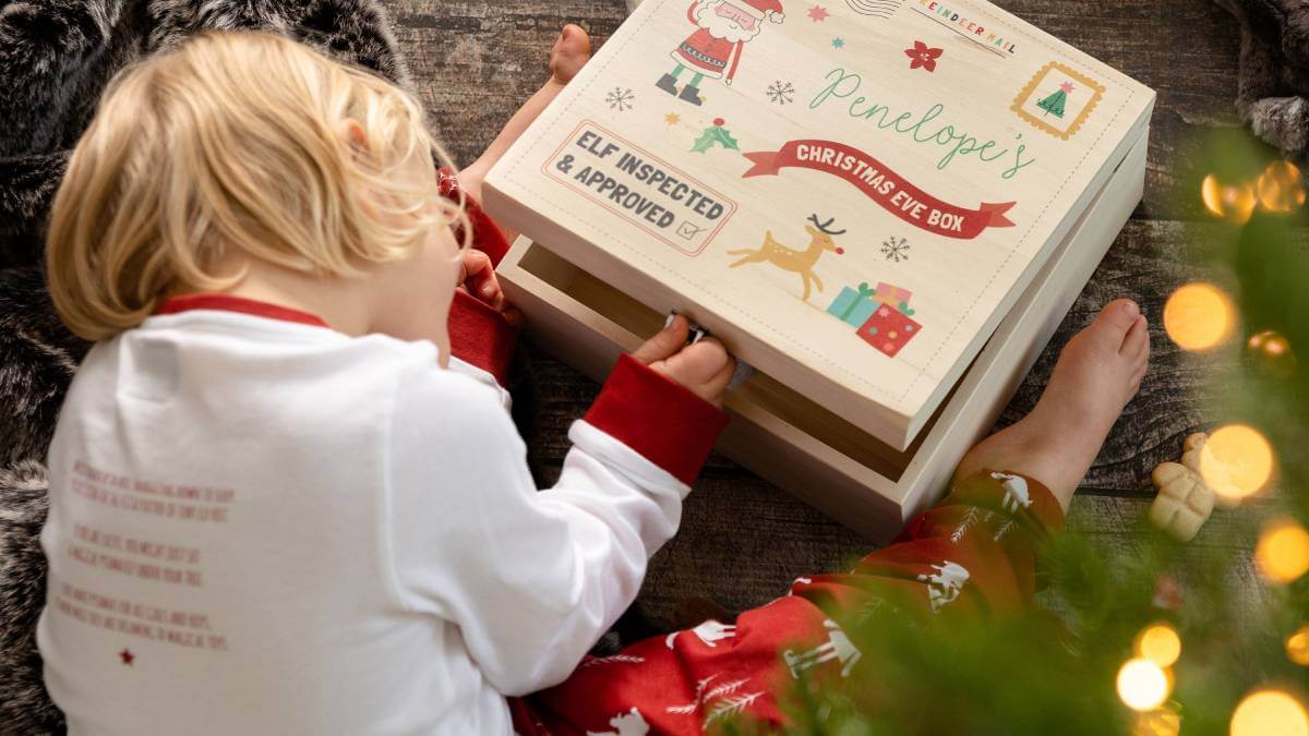 Child opening a Christmas Eve box next to a tree