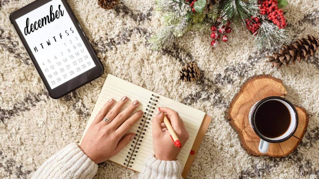Hands writing in a diary with a December calendar next to it