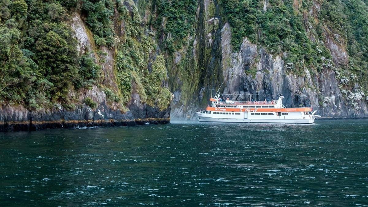 Cruise ship on water next to some cliffs
