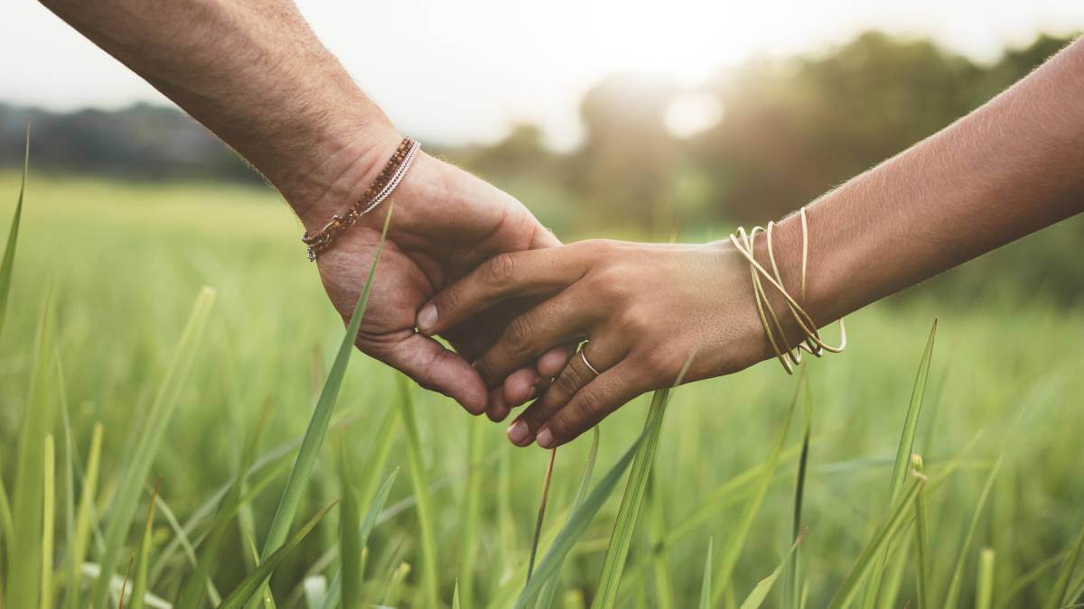 Two hands holding each other above green grass