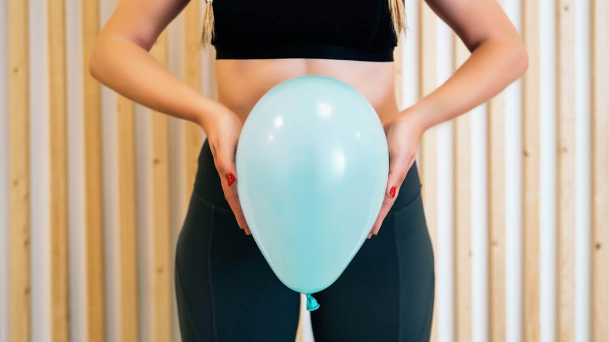 Woman holding a blue balloon in front of her pelvis