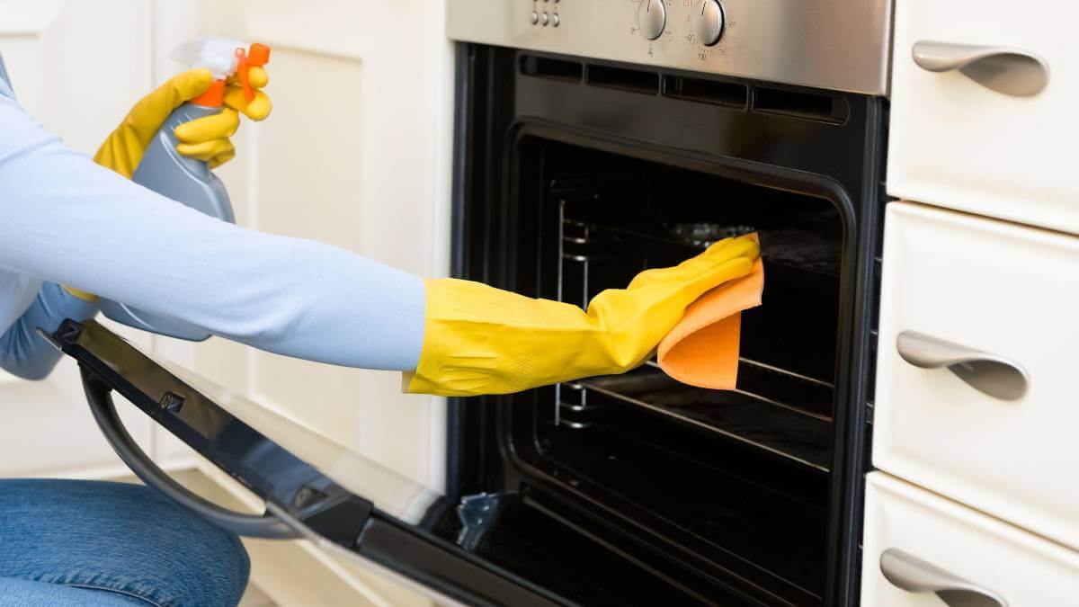 Women cleaning oven with yellow gloves and a spray bottle