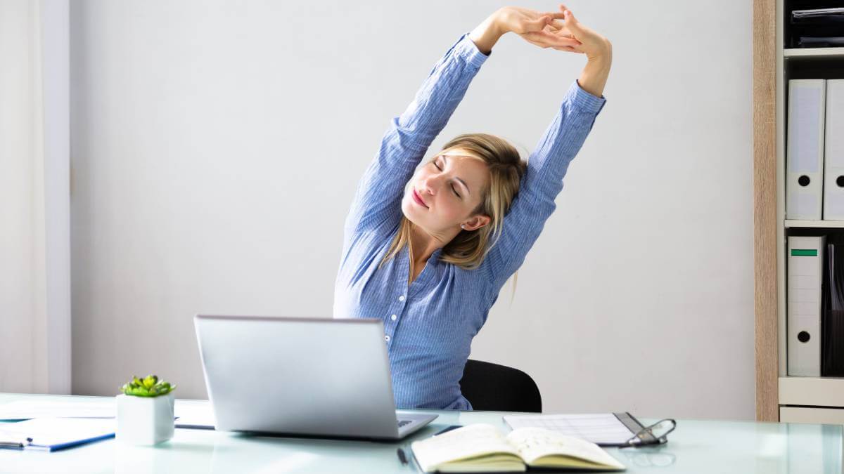 Woman sitting at a desk, stretching her arms in the air
