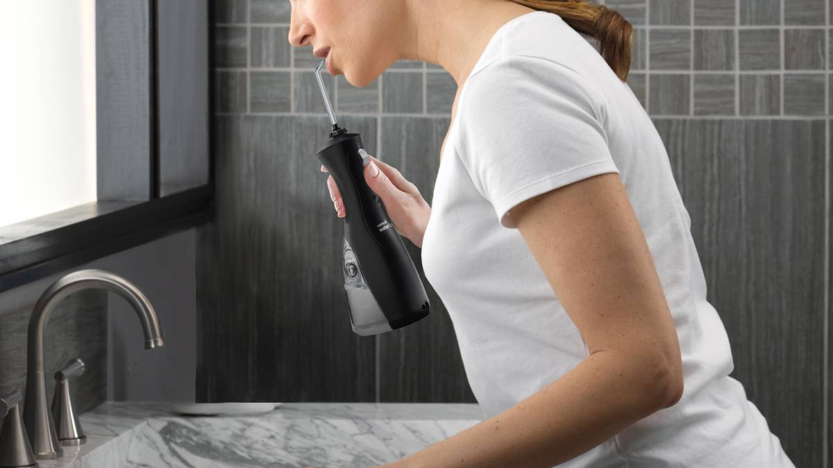 Woman using water flosser over bathroom sink