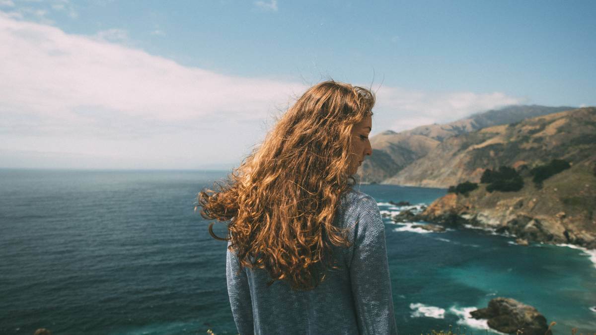 Woman with wavy hair standing next to the ocean