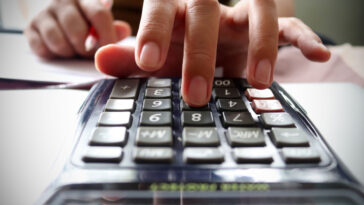 A woman's hand types superannuation fees costs into her calculator.