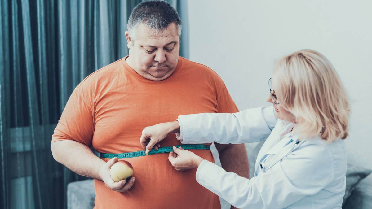 Overweight man getting his waist measured by a doctor
