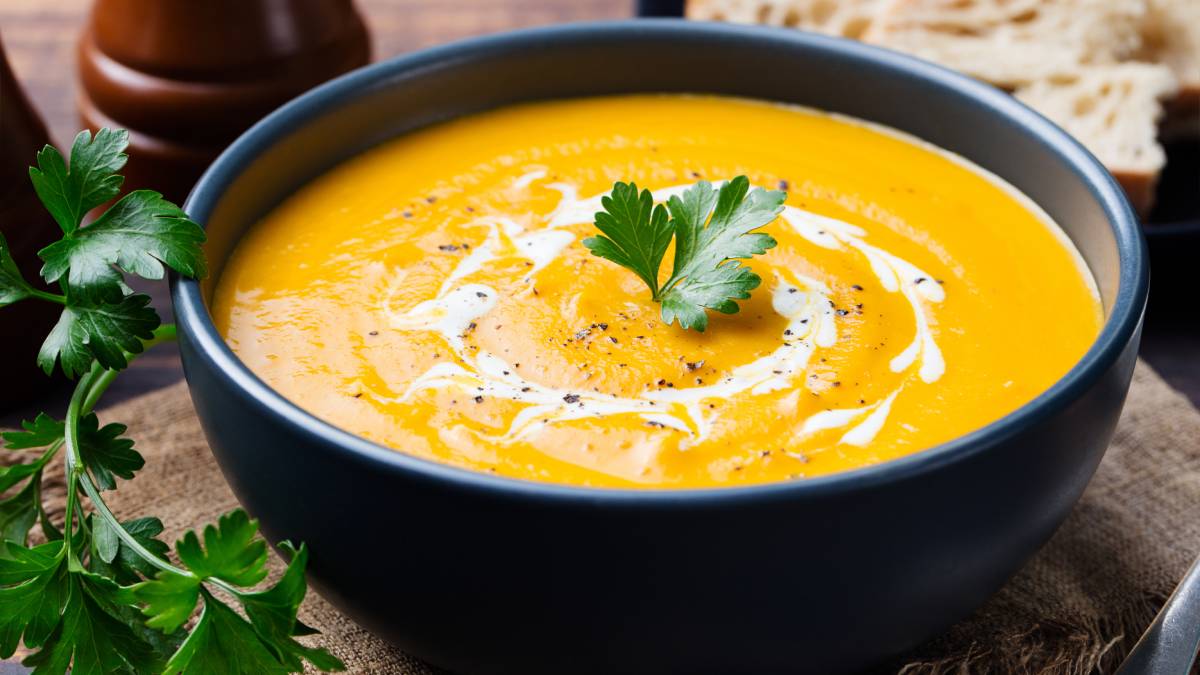 Pumpkin and carrot soup with cream and parsley on dark wooden background.