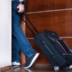 man walking out door with suitcase