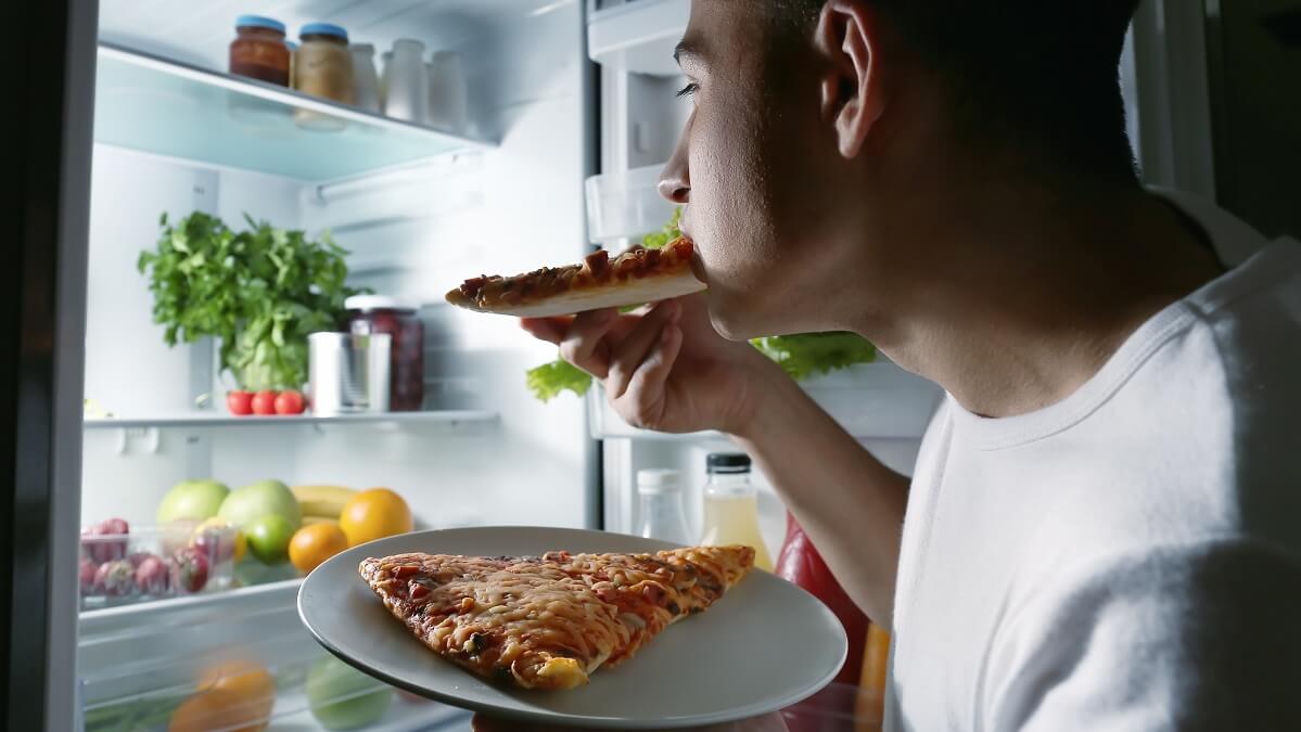 man eating snack from fridge at night