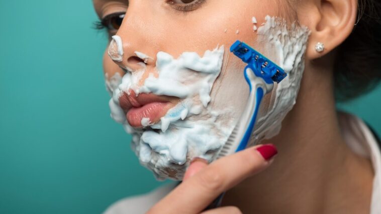 woman shaving face with razor